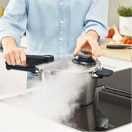 Person using a pressure cooker on a stove with steam rising