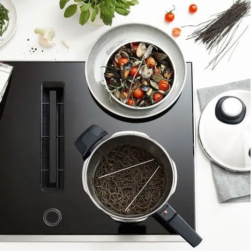 Stovetop with pots of food and ingredients on a white surface