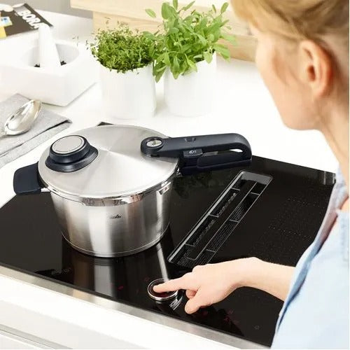 Stainless steel pressure cooker on a stovetop with a person interacting with it
