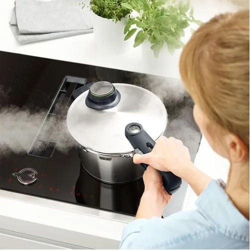 Person using a pressure cooker on an electric stove with steam rising