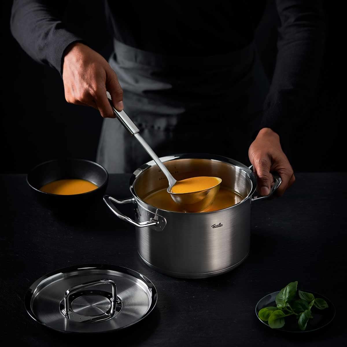 Person ladling soup from a pot into a bowl on a dark surface